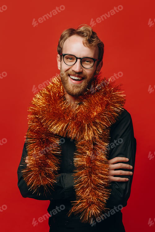 Preview: Red-haired cheerful man in glasses and golden boa at New Year party with confetti. Studio photo.