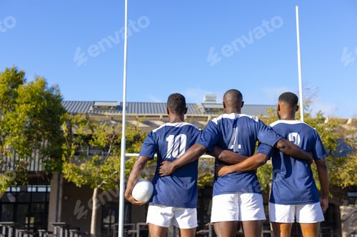 Preview: Three African American young male athletes wearing blue jerseys, standing on a rugby field outdoors
