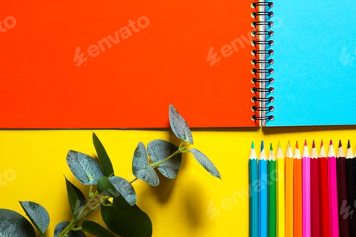 Preview: Rainbow palette of colored pencils with a spiral notebook on a yellow background