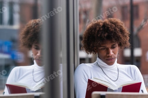 Preview: Relaxed young black man reading book in street cafe
