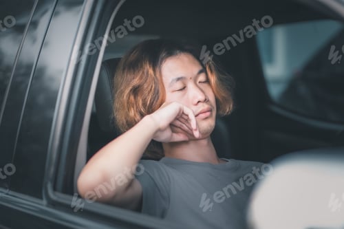 Preview: Young asian man with long hair sleeping in his car.