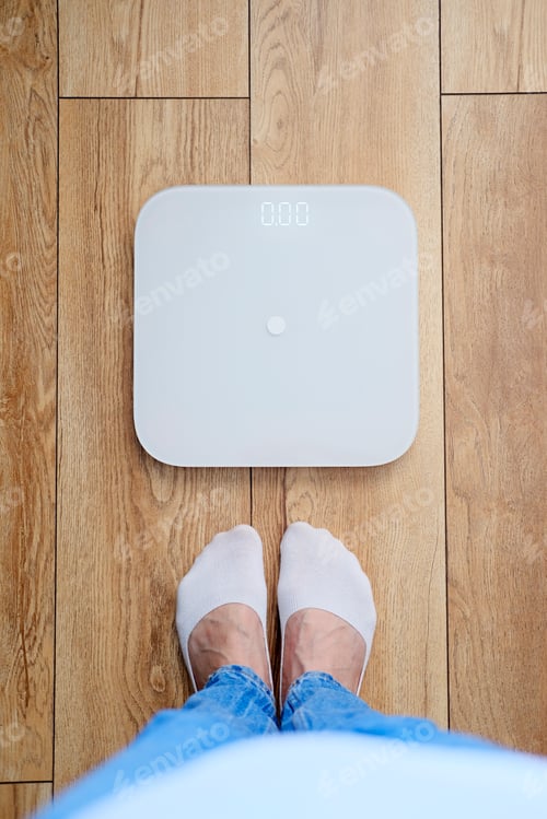 Preview: Woman in blue jeans weighing herself on floor scales