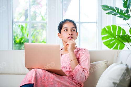Preview: Indian young female with a laptop sitting sofa in a modern living room