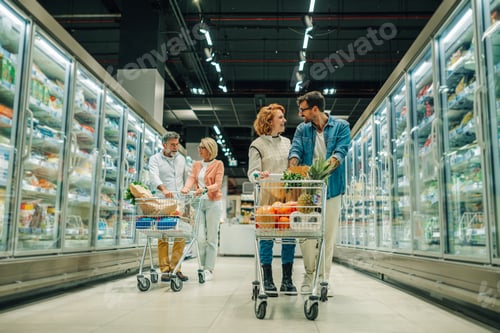 Preview: Happy couples shopping for groceries in supermarket, pushing carts down aisle