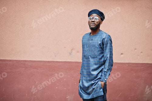 Preview: African guy in blue authentic costume, eyeglasses and beret. Fashionable nigerian man.