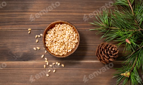 Preview: Pine nuts in a bowl on a brown wooden background with a branch of pine needles.