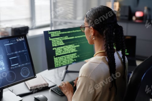 Preview: Female IT Developer with Glasses Looking at Multiple Computer Screens Working in Office