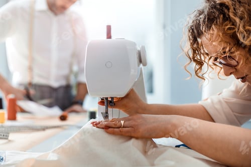 Preview: Professional dressmaker woman sews clothes on sewing machine at fashion design workshop