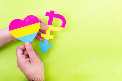Preview: Hands holding pansexual symbol and flag in the shape of a heart on green background with copy space