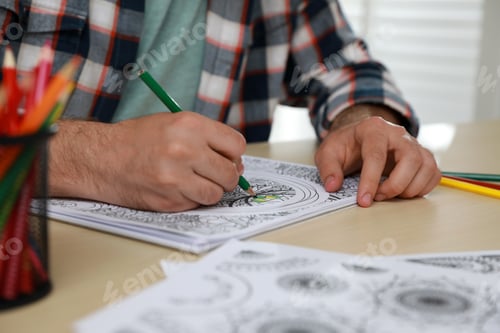 Preview: Man coloring antistress picture at table indoors, closeup