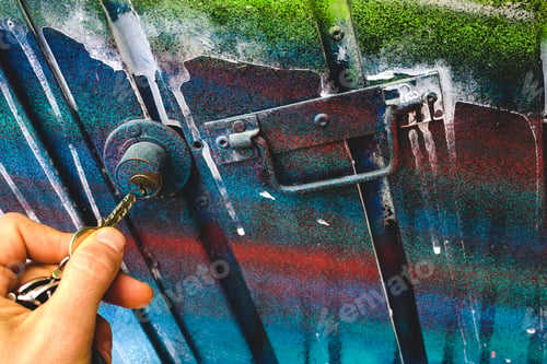 Preview: Man's hand using a key to open the lock of a door of an abandoned garage.