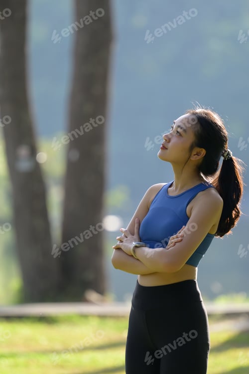 Preview: Young sportswoman looking up and thinking with arms crossed in a park