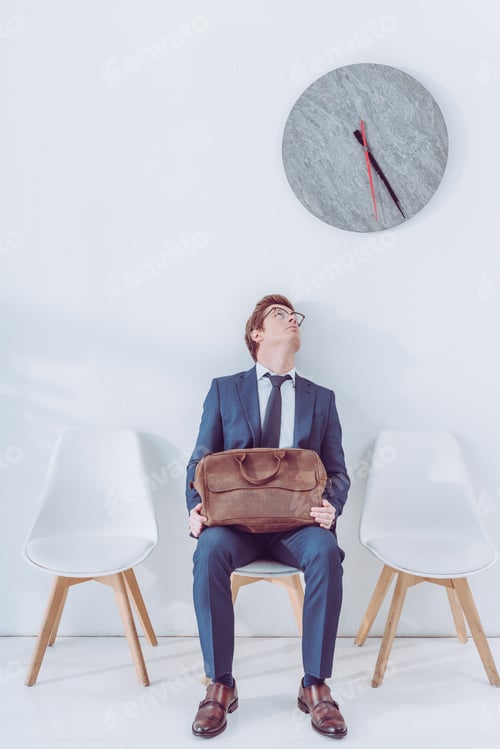 Preview: handsome employee in glasses holding briefcase and looking at clock