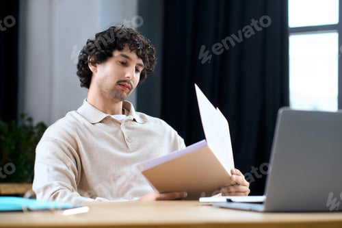 Preview: Handsome young man reviews important documents at a cozy desk in natural light