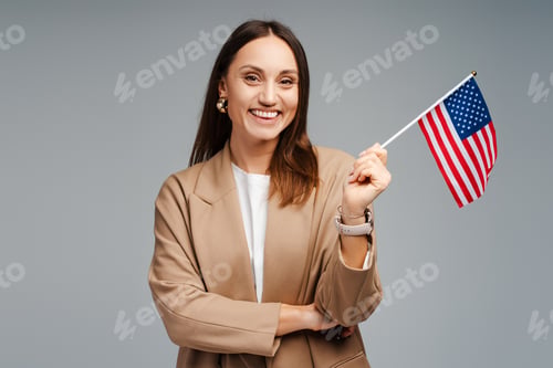 Preview: Portrait of happy young businesswoman showing American flag, isolated on graybackground