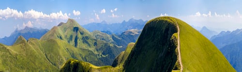 Preview: Panorama of green hills in summer mountains with gravel road for travelling by car