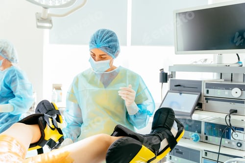 Preview: Medical assistant adjusting patient legs in surgical stirrups before gynecological procedure