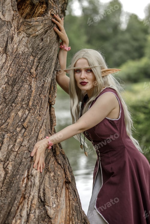 Preview: Young elf girl with blond long hair. Medieval elven princess in a burgundy dress in the forest