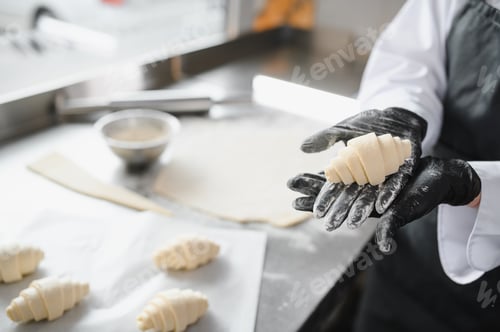 Preview: Baker showing freshly made croissant in hands wearing black gloves