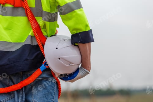 Preview: man engineer holding helmet safety wearing uniform standing at wind turbine field renewable energy.