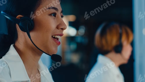 Preview: Asia young call center team using computer and microphone headset working in late night office.
