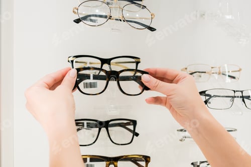 Preview: Close-up of woman choosing glasses on eyewear display stand in optical store.