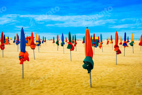 Preview: Lots of colorful closed umbrellas on the sunny summer beach with yellow sand