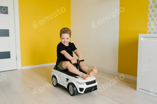 Preview: Child Boy Is Sitting in Toy Car, Smiling and Enjoying Himself in Room Is Brightly Lit and Has Yellow