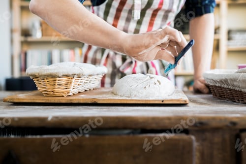 Preview: Midsection of baker making design on dough at table in bakery
