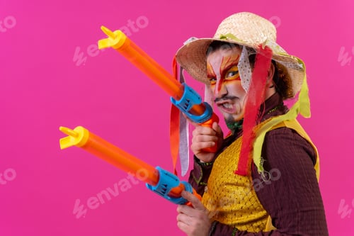 Preview: Juggler with white facial makeup on a pink background, smiling with toy guns and hat
