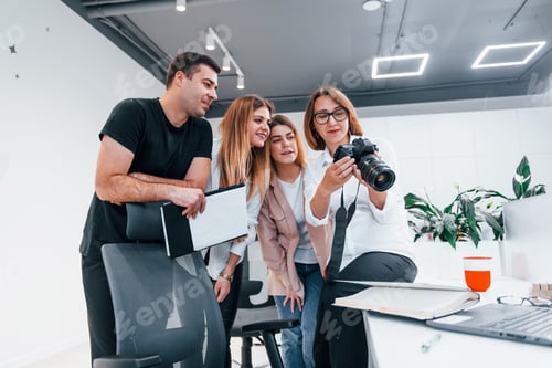 Preview: Group of business people in formal clothes indoors in the office looking at photos on the camera