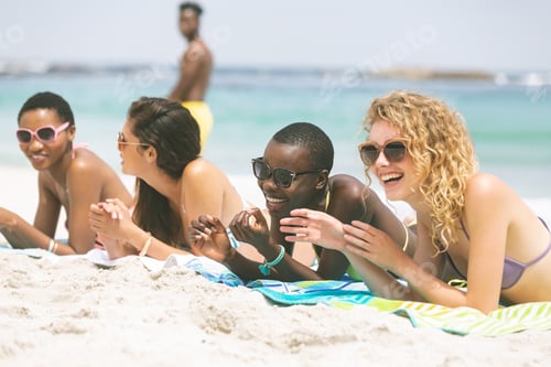 Preview: Front view of multi ethnic women interacting with each other while lying at beach on sunny day
