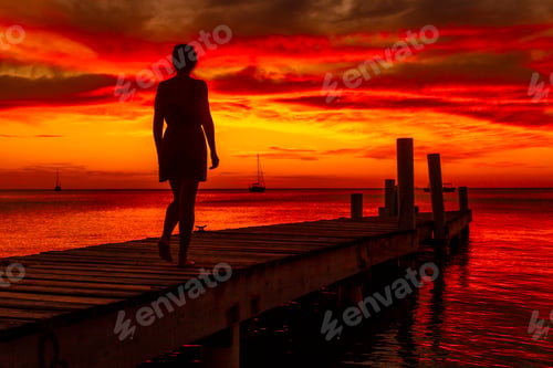 Preview: A young woman walking towards the Caribbean Sea in the orange sunset at the West End beach