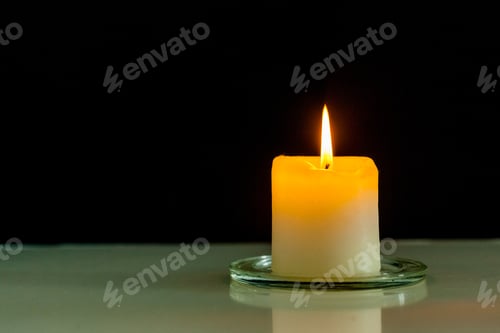Preview: Burning candle on a glass dish with a black background during nighttime