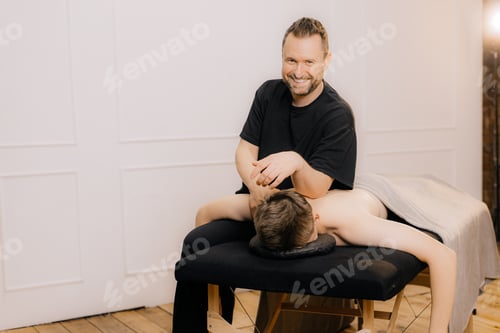 Preview: Smiling Man Massaging Young Adult on Table