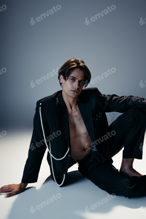 Preview: stylish man in suit with pearls and hairy chest sitting on dark grey background