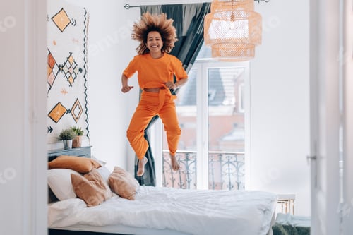 Preview: young african american woman dressing casual orange jumping for joy over bed
