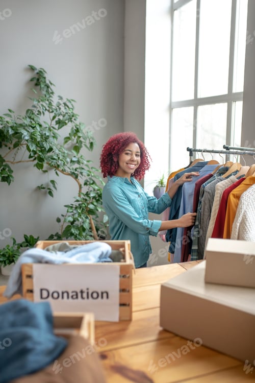 Preview: Young smiling girl standing in room and looking at shirt.
