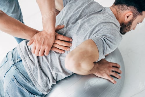 Preview: chiropractor massaging back of man lying on fitness ball
