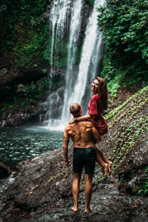 Preview: A man holds a woman in his arms at the waterfall. Couple at the waterfall, rear view