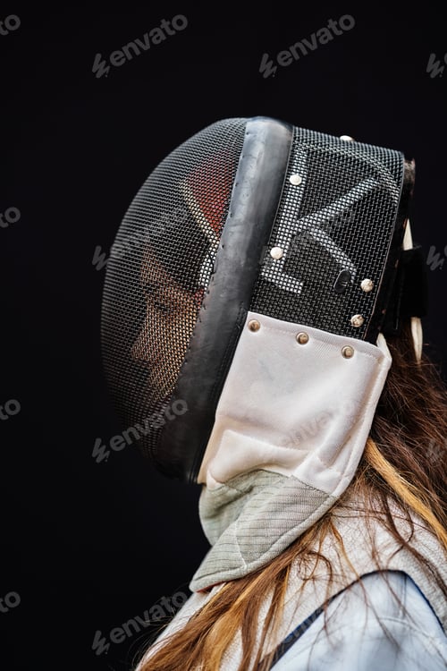Preview: Portrait of woman dressed in white fencing costume practicing with the sword on black background.