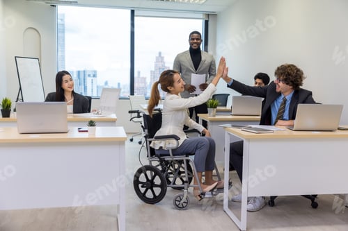 Preview: Office workers and woman on a wheelchair in bright office. They are showing a teamwork.