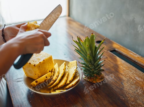 Preview: Freshly sliced pineapple on a wooden table with a person cutting up a ripe pineapple fruit