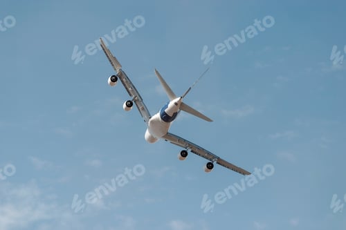 Preview: Large passenger jet is banking against a beautiful blue sky with a few white clouds.