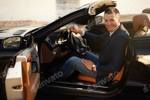 Preview: Young businessman in luxury convertible car outdoors