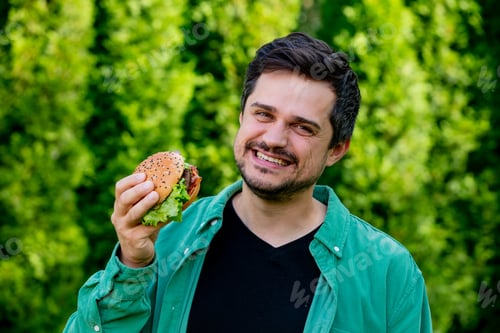 Preview: Casual man in green shirt with burger in outdoors
