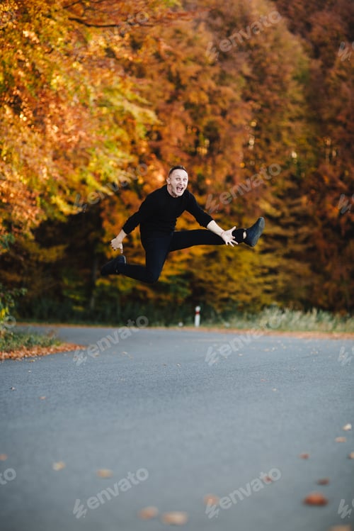 Preview: Young attractive man is having fun on road in autumn forest. Guy with short hair wearing in black