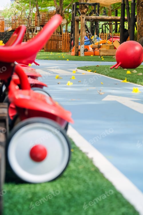 Preview: Red tricycles line up beside a track in a children's playground area