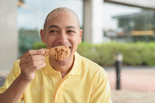 Preview: Bald Hispanic man eating fried chicken for lunch during day outdoors close-up shot