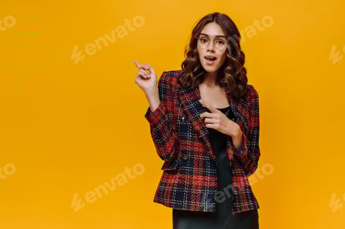 Preview: Shocked lady in glasses and striped outfit showing to place for text on isolated backdrop. Wavy hai